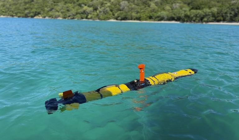 黄色的圆柱形IVER3-AUV漂浮在清澈的蓝绿色水中.